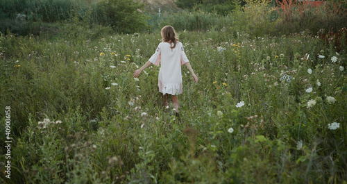Blonde girl in pink linen dress walks in the field of flowers summer 