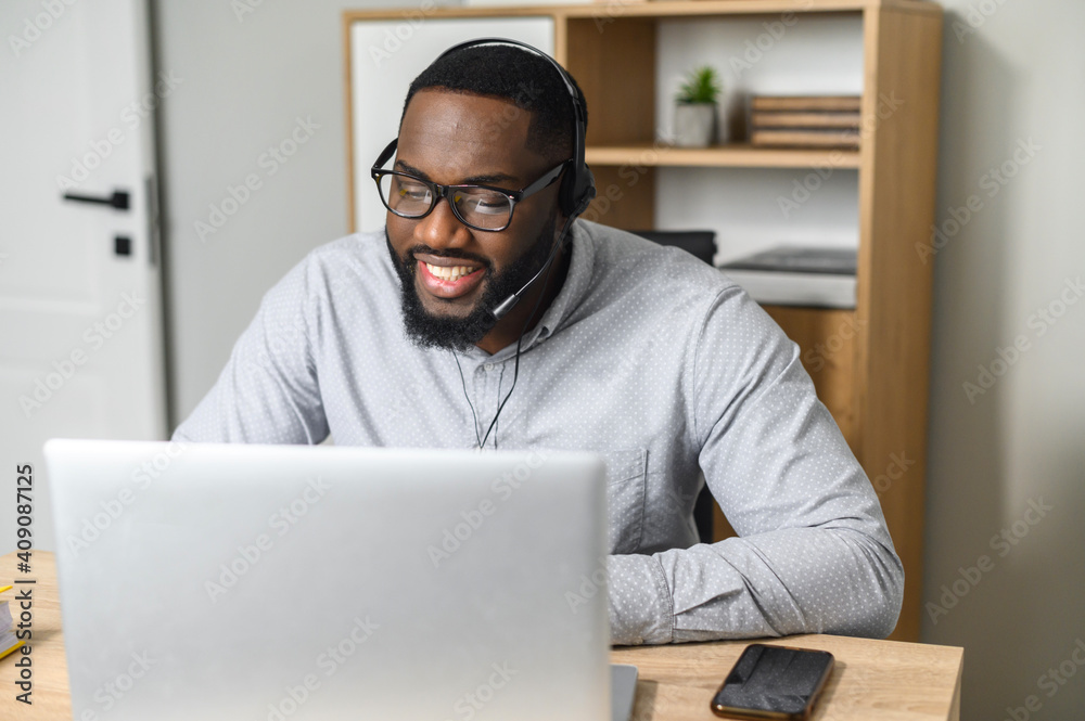 An excited young African-American office worker in glasses going live and streaming webinar. Professional teaching students at online conference, using the laptop to present a project, and talking An excited young African-American office worker in glasses going live and streaming webinar. Professional teaching students at online conference, using the laptop to present a project, and talking