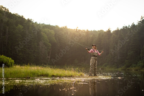 Woman angler fly-fishing in NH backcountry lake during afternoon light photo