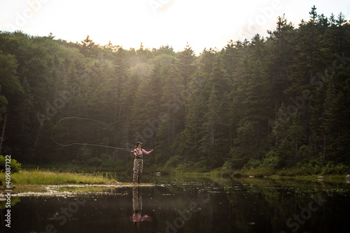 Woman angler fly-fishing in NH backcountry lake during afternoon light photo