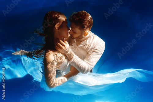 Couple kissing or hugging in the water. A girl in a dress with a long train and a guy are swimming in the water.