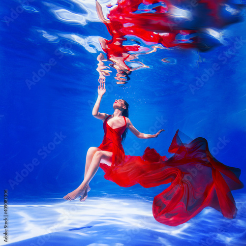young woman in a red dress on the water. Girl swims in the water in a dress with a long train