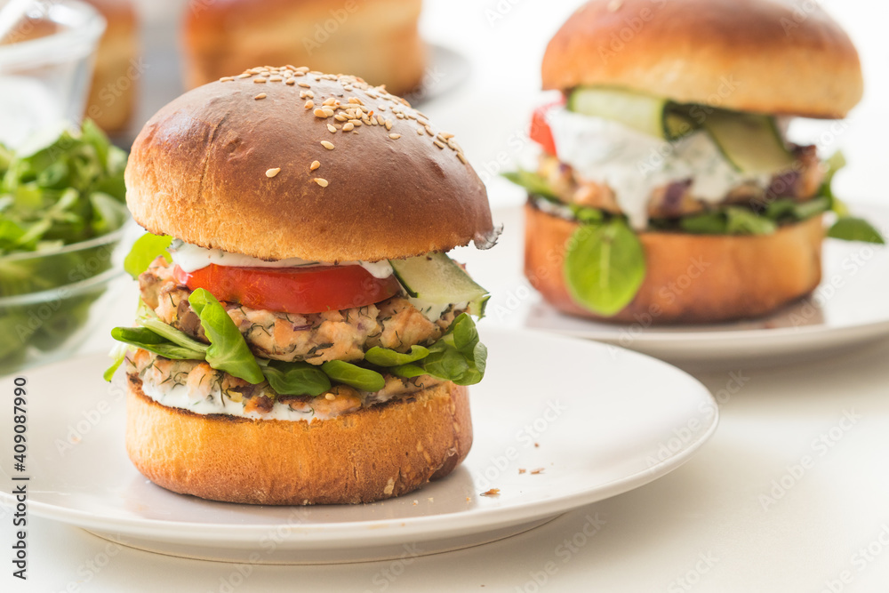Two portions of fresh, homemade salmon burgers on white plate Two portions of fresh, homemade salmon burgers on white plate