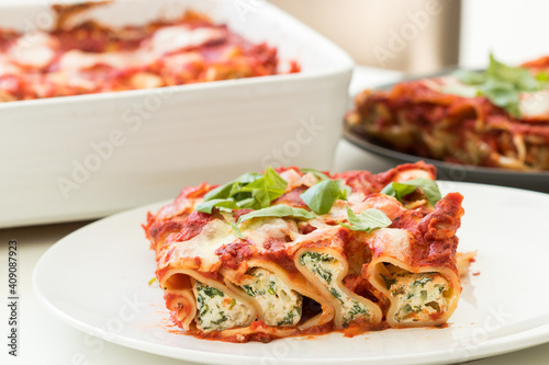 Freshly cooked cannelloni pasta filled with spinach and ricotta, served on white plate with fresh basil
