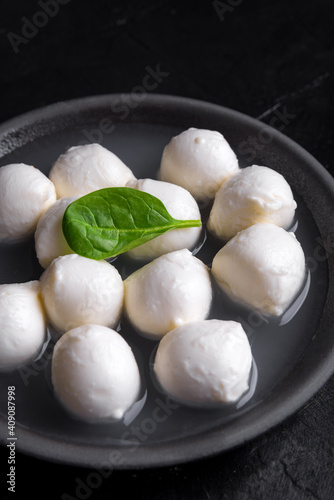 Traditional Italian Mozzarella cheese and basil on rough ceramic plate and black background. Selected focus.