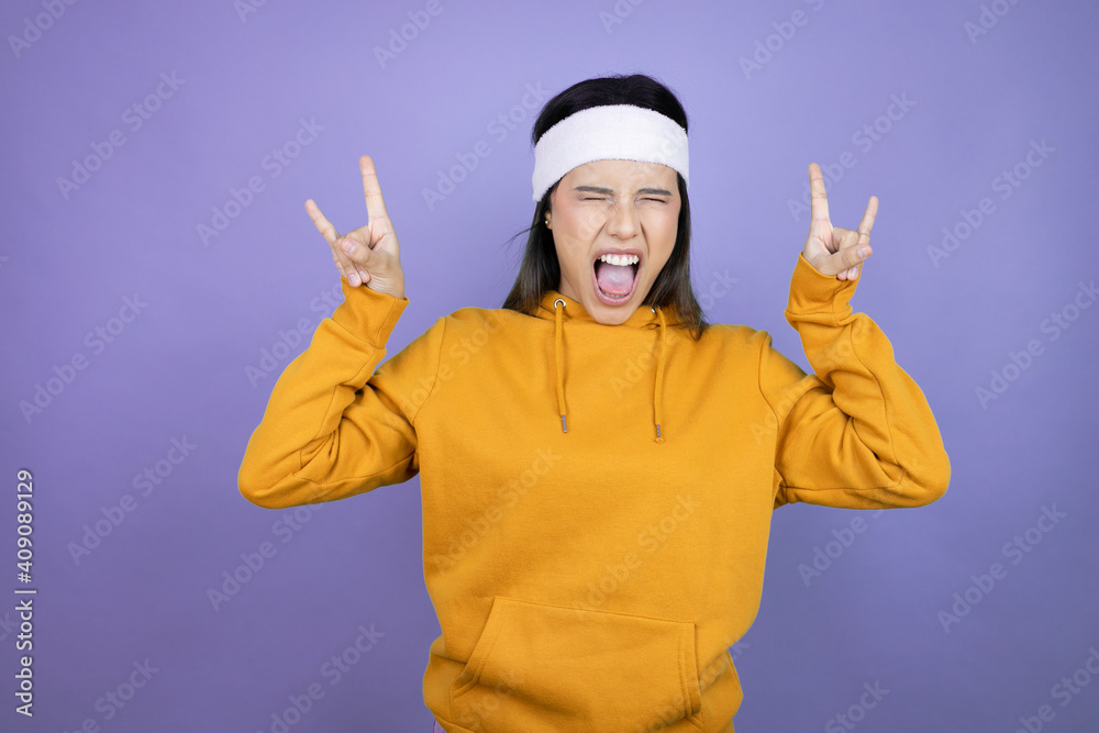 Young latin woman wearing sportswear over purple background shouting with crazy expression doing rock symbol with hands up