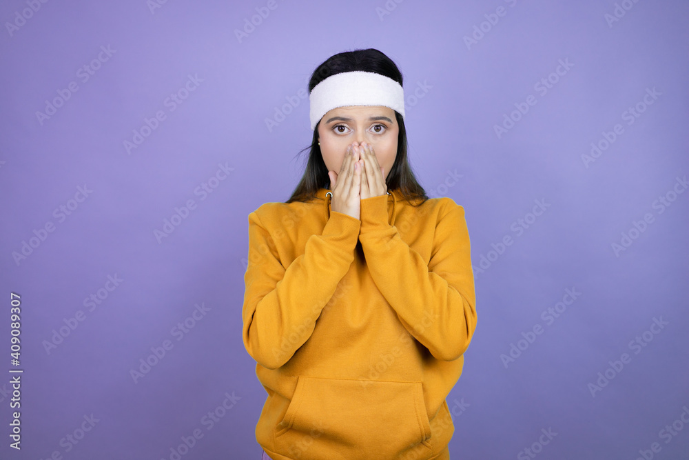 Young latin woman wearing sportswear over purple background shocked covering mouth with hands for mistake. secret concept.