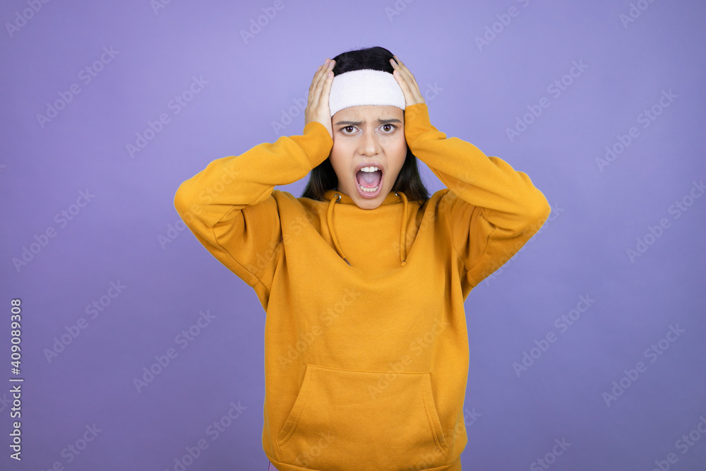 Young latin woman wearing sportswear over purple background crazy and scared with hands on head, afraid and surprised of shock Young latin woman wearing sportswear over purple background crazy and scared with hands on head, afraid and surprised of shock