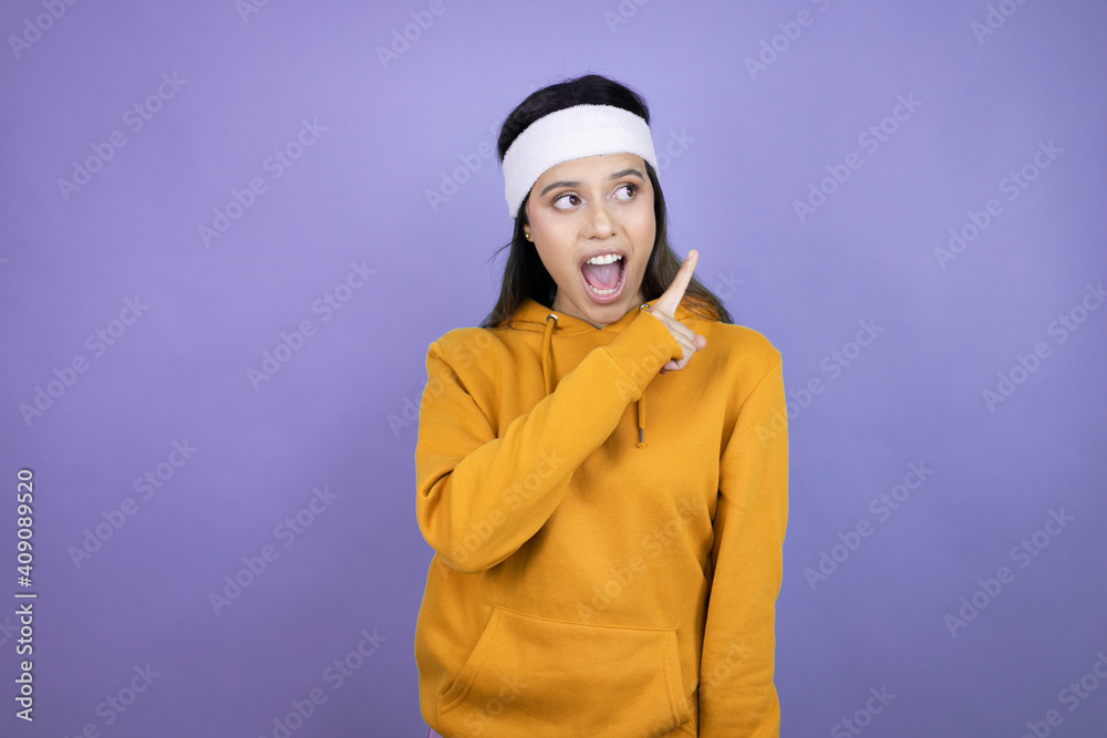 Young latin woman wearing sportswear over purple background smiling and pointing with hand and finger to the side Young latin woman wearing sportswear over purple background smiling and pointing with hand and finger to the side