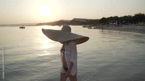 Middle shot of girl in a big hat walking near the sea of Greece. Young woman wearing a big hat and sunglasses is walking on the coastline of Khalkidhiki island and watching the sunset. High quality photo