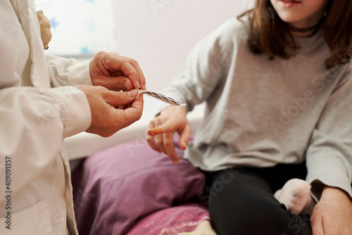 Close-up of a female doctor placing a band-aid on a girl's finger on her bed. Home doctor concept