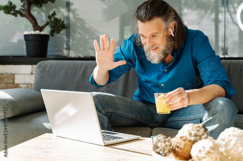 Mature man with a beard drinking orange juice and looking at his lapto photo