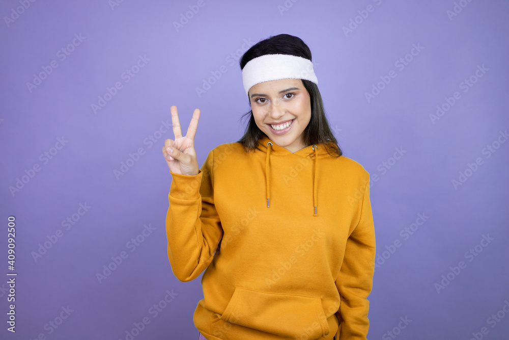 Young latin woman wearing sportswear over purple background showing and pointing up with fingers number one while smiling confident and happy Young latin woman wearing sportswear over purple background showing and pointing up with fingers number one while smiling confident and happy