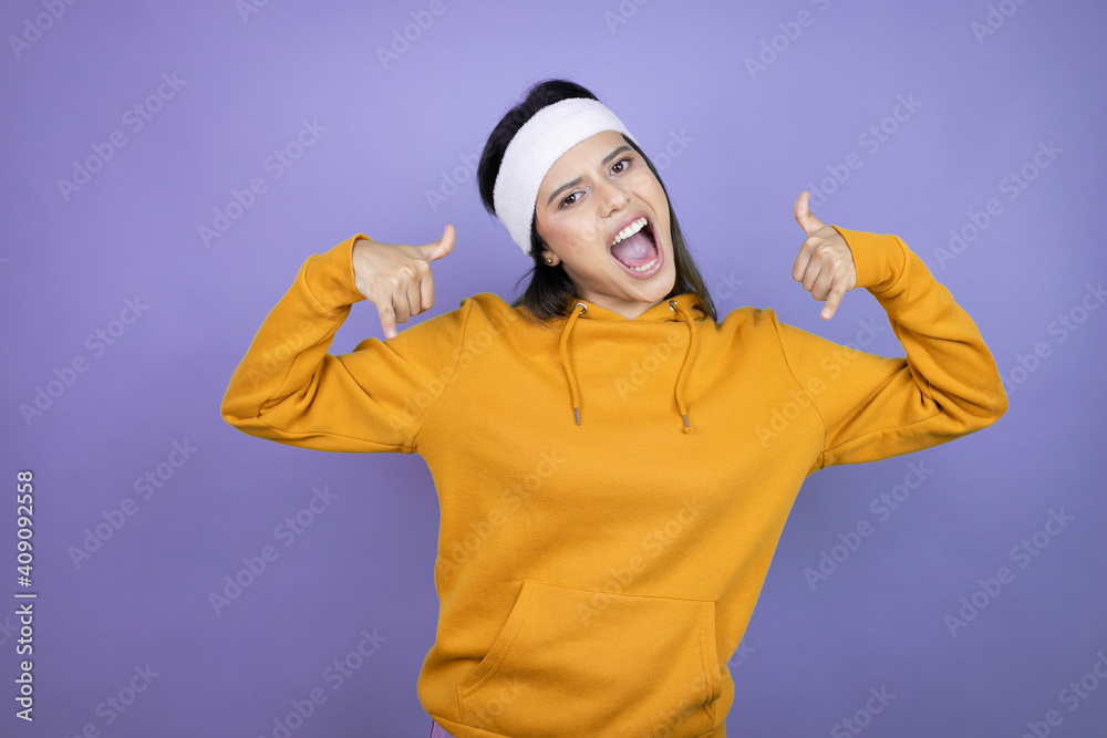 Young latin woman wearing sportswear over purple background shouting with crazy expression doing rock symbol with hands up Young latin woman wearing sportswear over purple background shouting with crazy expression doing rock symbol with hands up
