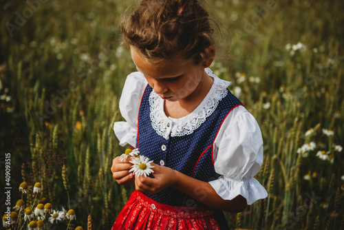 Beautiful girl collecting flowers in the field wearing a German Dirndl photo