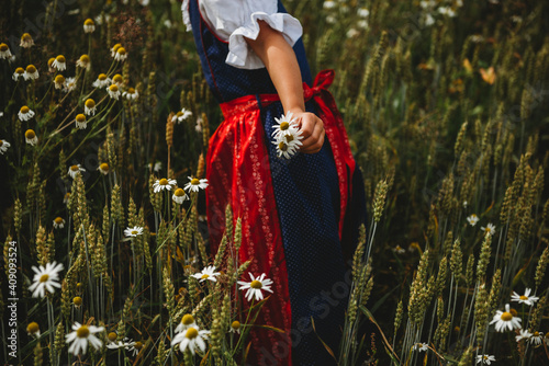 Girl wearing traditional dress picking daisies at field on sunny day photo