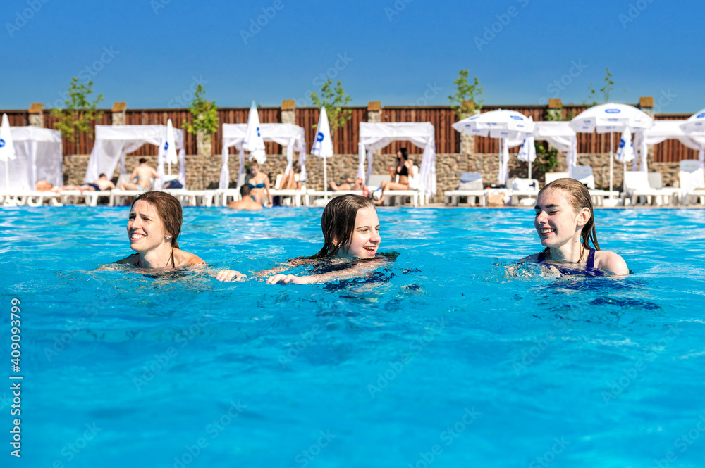 Three girls swim in a pool with blue water. Teens having fun and enjoying in swimming pool