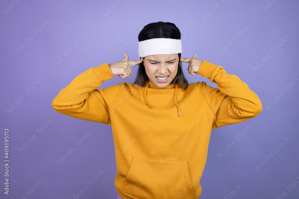 Young latin woman wearing sportswear over purple background covering ears with fingers with annoyed expression for the noise of loud music. Deaf concept. Young latin woman wearing sportswear over purple background covering ears with fingers with annoyed expression for the noise of loud music. Deaf concept.