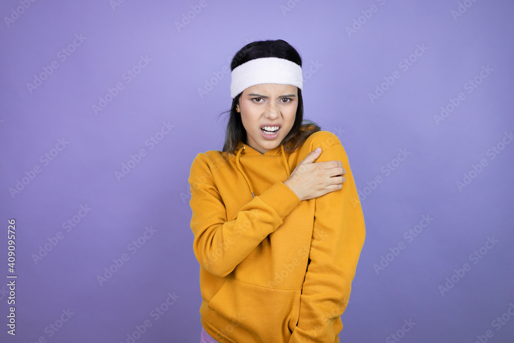 Young latin woman wearing sportswear over purple background with pain on her shoulder and a painful expression