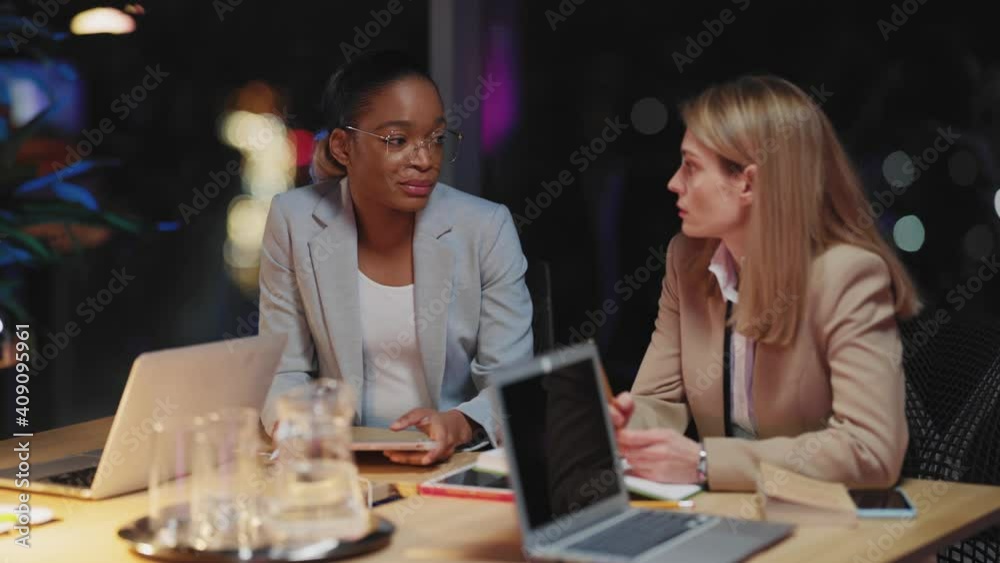 Young couple of business women sitting together in boardroom, talking about life and business, participating in company meeting in late evening. Young couple of business women sitting together in boardroom, talking about life and business, participating in company meeting in late evening.