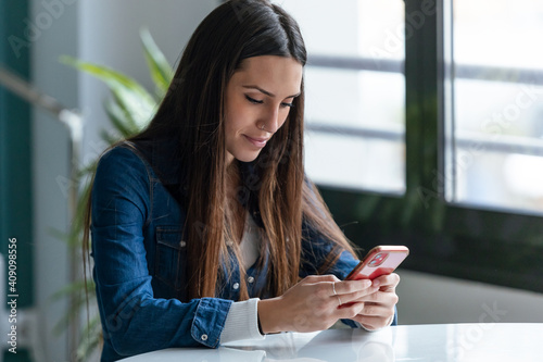 Smiling young business woman sending messages with mobile phone while working in the desk at home.