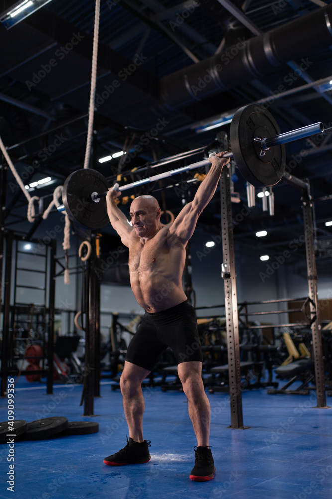 Elderly athlete doing snatch exercise in gym