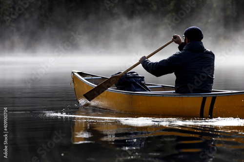 Focused man paddles canoe into fog on a tranquil lake