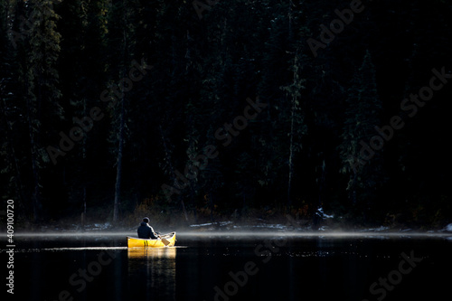 Rugged man solo paddles canoe on misty calm lake by thick forest photo