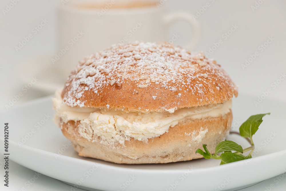 Finnish Shrovetide bun (laskiaispulla) close up on a white plate with a mint leaf. Finnish Shrovetide bun (laskiaispulla) close up on a white plate with a mint leaf.