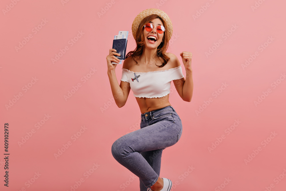 Obraz premium Slender beautiful girl jumps and dances from happiness, rejoicing at accomplished trip abroad. Studio photo of pretty woman laughing in pink round glasses