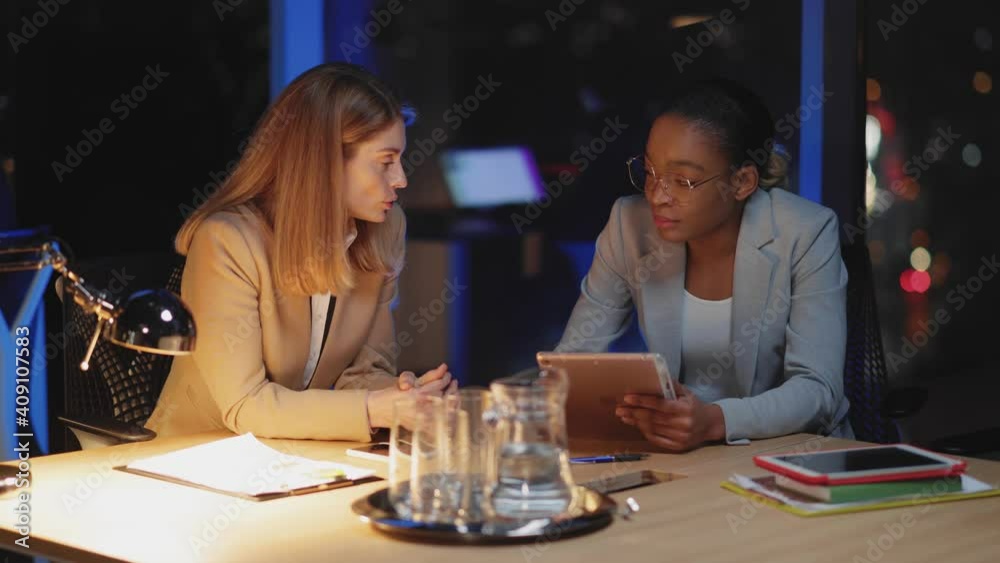 Workaholic couple of pretty female managers sitting together in boardroom negotiating creative ideas brainsotmring using tablet for management. Workaholic couple of pretty female managers sitting together in boardroom negotiating creative ideas brainsotmring using tablet for management.