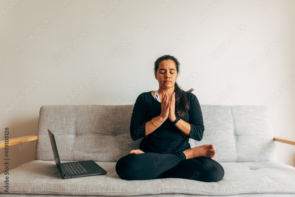 Latin woman sitting doing yoga watching an online class indoors. Yoga at home concept. Copy space