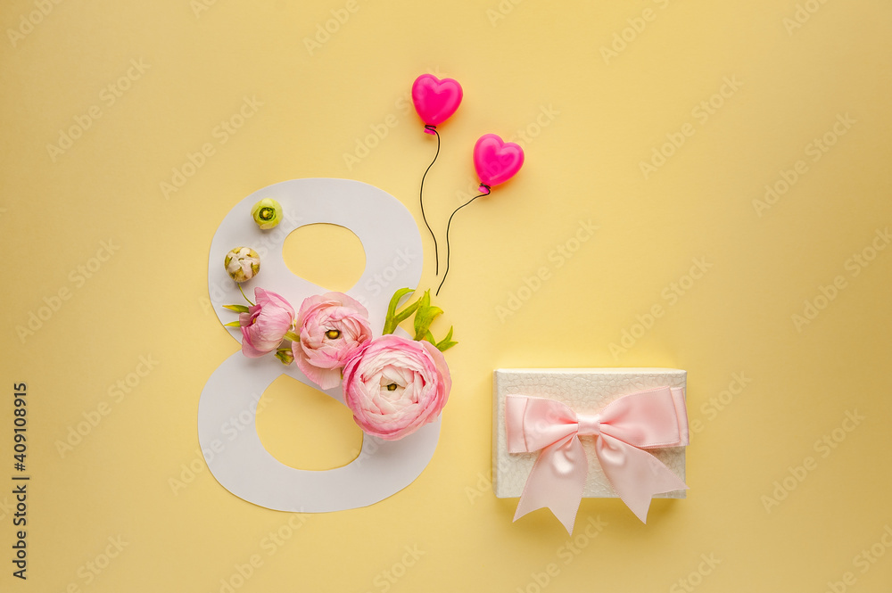 Fototapeta premium Greeting Card International Women's Day on March 8th. Pink ranunculus decorates the number eight and gift box with bow on yellow background. Soft focus. Top view.