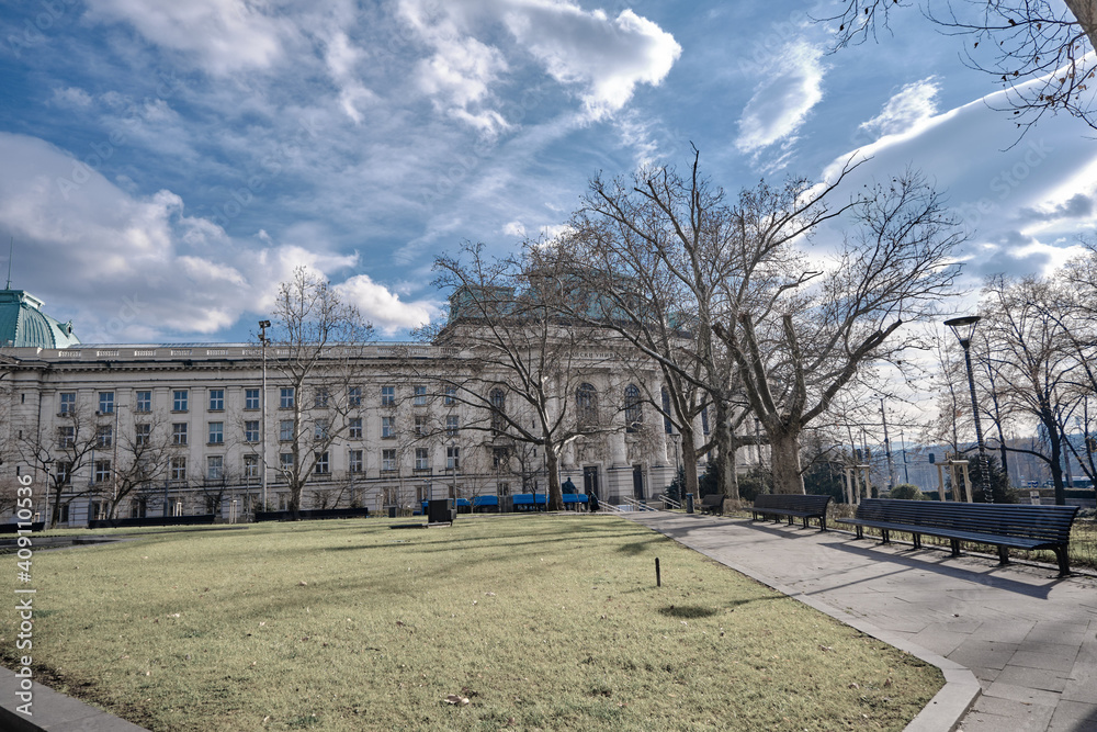 Fototapeta premium Sofia university view from small cute city park with sunshine coming from clouds. Bulgaria. Sofia. 06.01.2021.