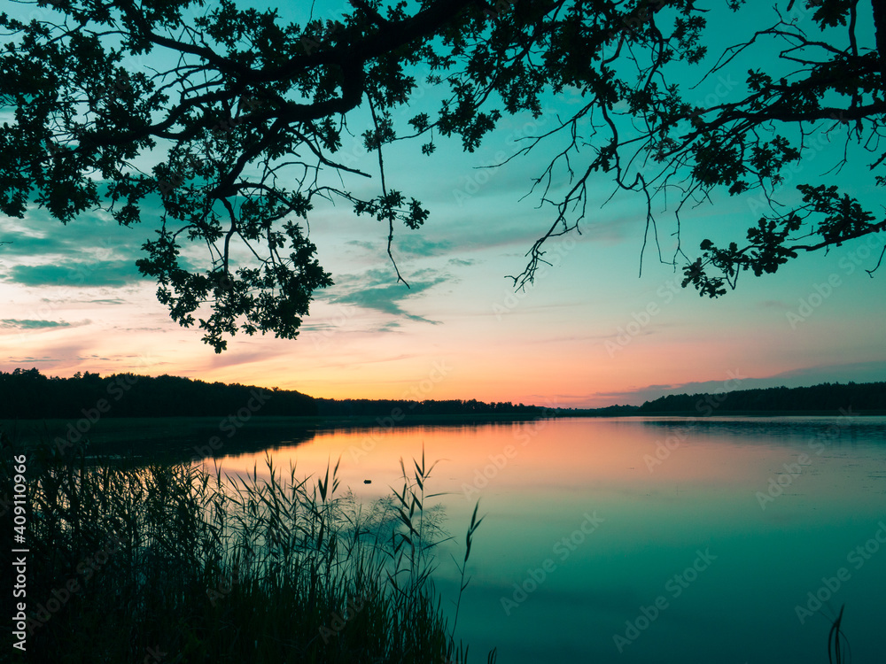 Sunset reflection landscape on Masuria. Dark oak tree branches. Seksty lake.  Blue and orange