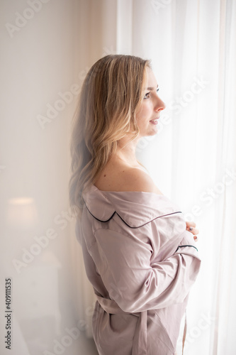 Brunette in mens shirt. Rear view of young woman looking through the window in the morning