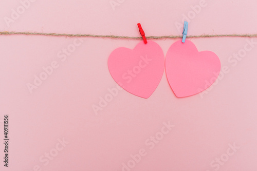 Clothes pegs and red paper hearts on rope isolated on pink background