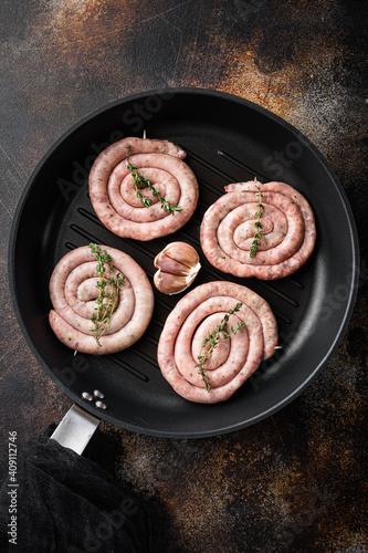 Raw meat sausage in cast iron frying pan, on old dark rustic background, top view flat lay