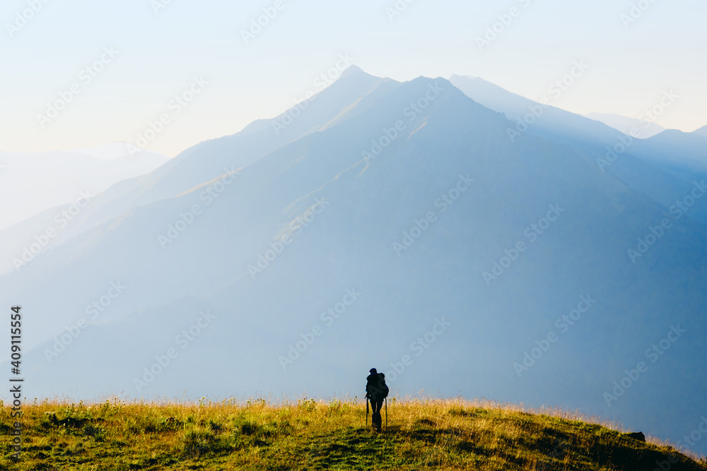 Silhouette of a lonely traveler at sunrise on the background of a high mountain	