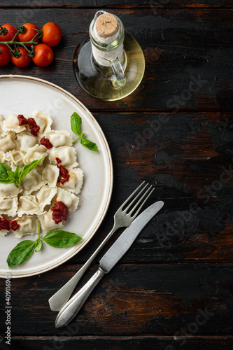 Appetizing ravioli with tomato sauce, cheese and basil with basil parmesan and tomatoe on white plate on old dark  wooden table background , top view flat lay , with copyspace  and space for text