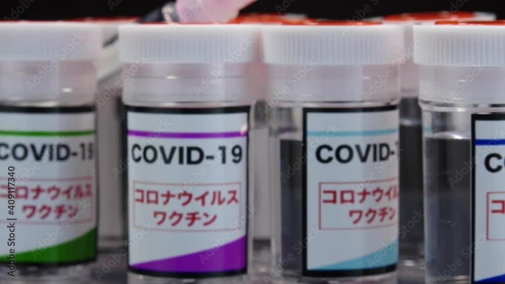 CORONAVIRUS (COVID-19) VACCINE and syringe in laboratory. Colorful glass bottle of liquid remedy for injection use. Manufacture drugs for medical supplies of pharmacy industry. Label in Japanese word. CORONAVIRUS (COVID-19) VACCINE and syringe in laboratory. Colorful glass bottle of liquid remedy for injection use. Manufacture drugs for medical supplies of pharmacy industry. Label in Japanese word.