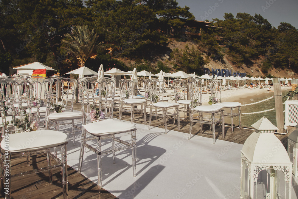 White wedding chairs decorated with fresh flowers in restaurant with panoramic sea view. Luxury design for events. Background for celebrations and ceremonies. Perfect image for creativity. Copy space