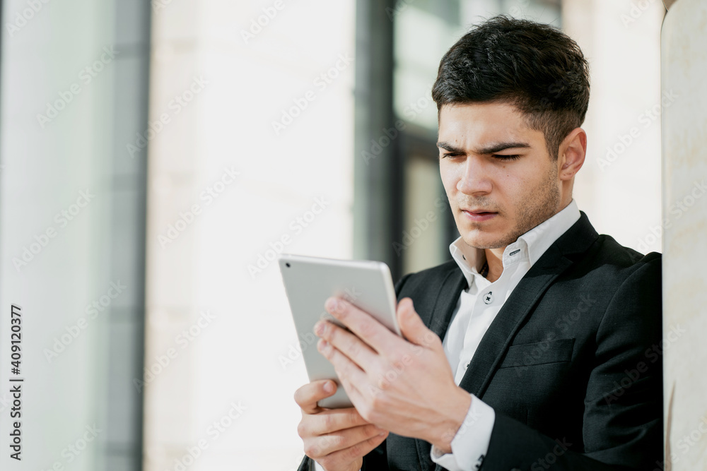a serious manager is a business employee working in a business center in a bank. dark-haired European appearance. business suit and white shirt. copy space. holds a tablet and writes a message.