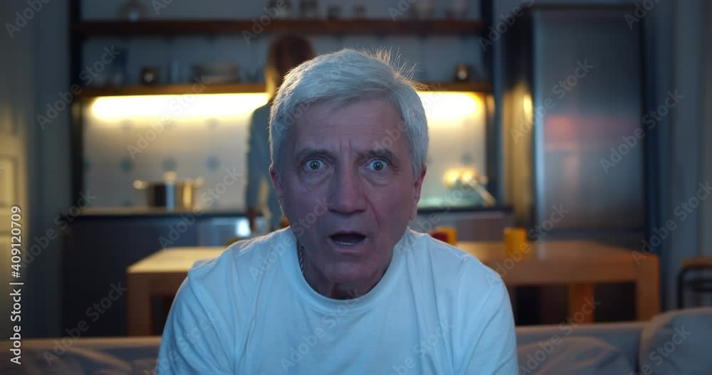 Shocked senior man sitting on sofa watching interesting tv show Shocked senior man sitting on sofa watching interesting tv show