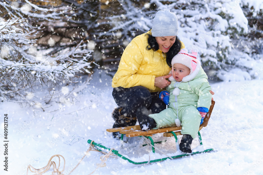 mother and child walks in the winter forest, mom rides a baby on a sled, bright snowy fir trees, beautiful nature