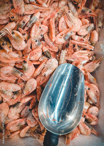 Top view of frozen prawns and metal scoop in market. Deepfrozen pink shrimps, vertical orientation photo