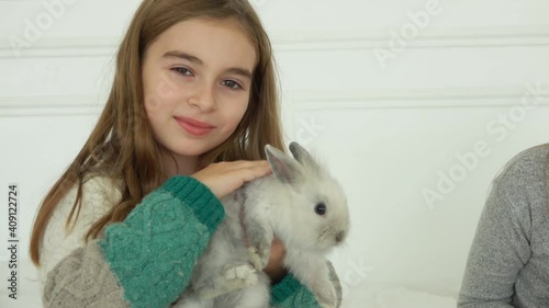 The happy smiling girl is caressing a cute grey fluffy little rabbit 