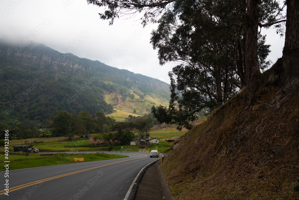 Truck and car on a highway curve in a Colombian country landscape with mountains and mist descending in the morning. Colombia.