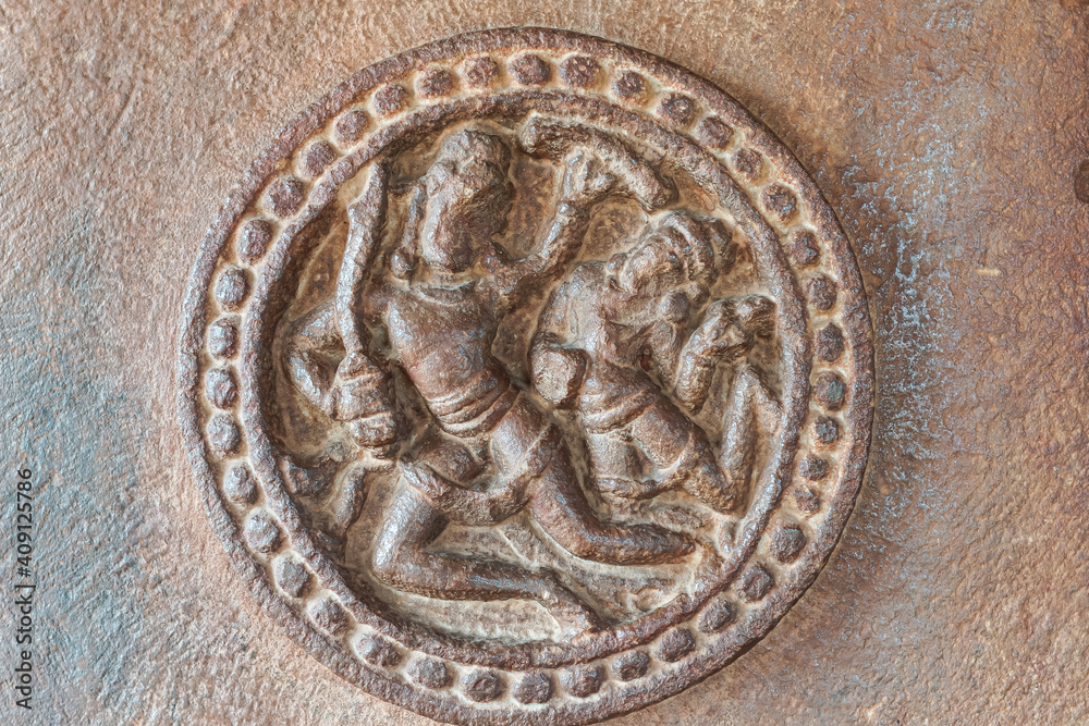 Aihole, Karnataka, India - November 7, 2013: Durga Gudi or Temple. Closeup of brown stone, 2 human figures sculpture captured in circular decoration but faces damaged.