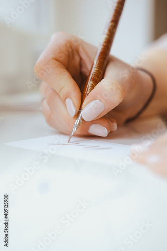 A hand with pen creates a business card with a calligraphic letter